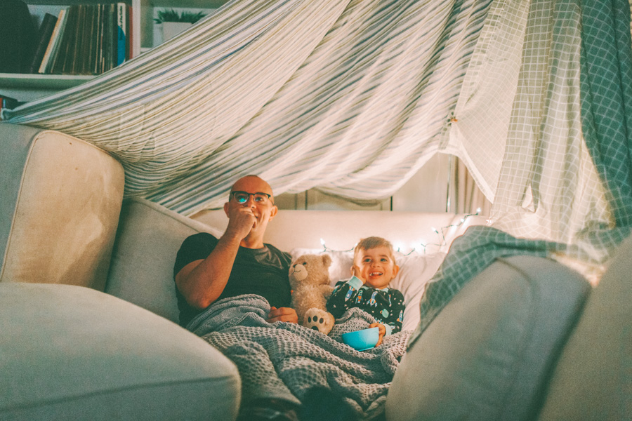 dad and toddler watching TV under a fort