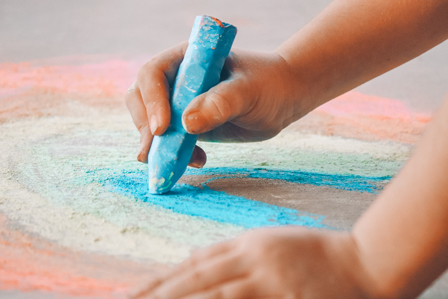 toddler hands playing with sidewalk chalk and making a rainbow