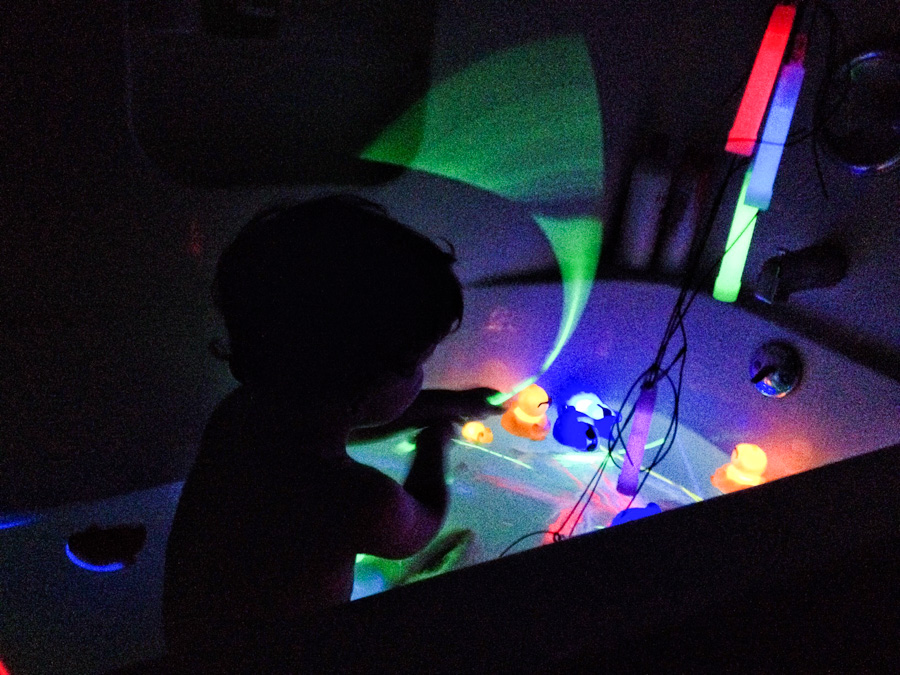 toddler in a bath with glow sticks in a dark room