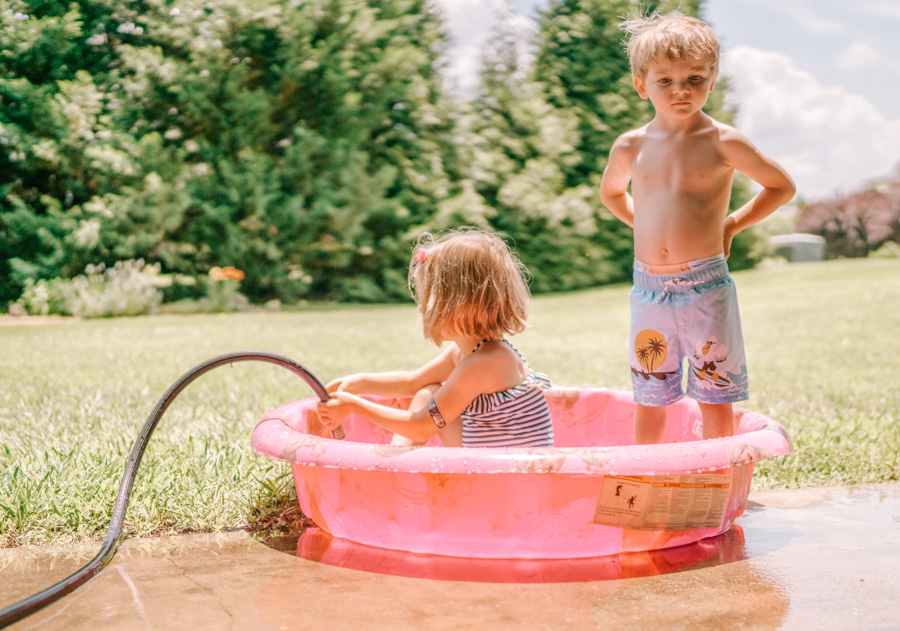 2 kids in pink kiddie pool in a yard