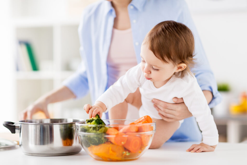 happy mother and little baby girl with vegetables and pot at home kitchen